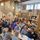 Creative Forum at Pop Recs Groups of people sit at long wooden tables talking amongst one another with coffees, large sheets of paper and pens. The room has bare concrete walls and a yellow beam through the middle. At the back is a plywood wall that has large black text on it reading 'Hunger Melody Decency'.