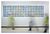 Commissioned by Newcastle RVI Glass artwork mounted on a white wall. The artwork is a rectangle made up of individual glass sculptures of different coloured irises with a black pupil at the centre of each. There are 25 small sculptures across and 7 down. There are blurred figures walking across the space in front of the artwork.
