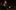 Sandrin-aspect-ratio-16-9 A person with a black shirt, dark short hair and a beard. They are holding their hands up in front of them.