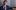 Callum-McLachlan-2-aspect-ratio-16-9 A person sat wearing a blue suit, white shirt and burgundy tie. They have short brown hair and their left arm rest on a musical instrument.