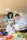 Puppet Making Workshop | Culture Start Two people working together on an art project in a bright classroom. A person with curly dark hair wears a blue shirt and a white apron with colorful pom-poms and stars. The apron has
