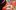 Arty-Fridays-Clay-Creations-aspect-ratio-16-9 A female child with very dark brown hair with a pink headband sits at a desk modelling a clay pot. The table has a red tablecloth. The tablecloth has teddy bears printed over the red.