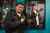 Autonomy Photography project A person with short dark hair and a black jacket holds a professional camera. They stand in front of a teal wall with a large framed portrait of themselves holding the same camera.