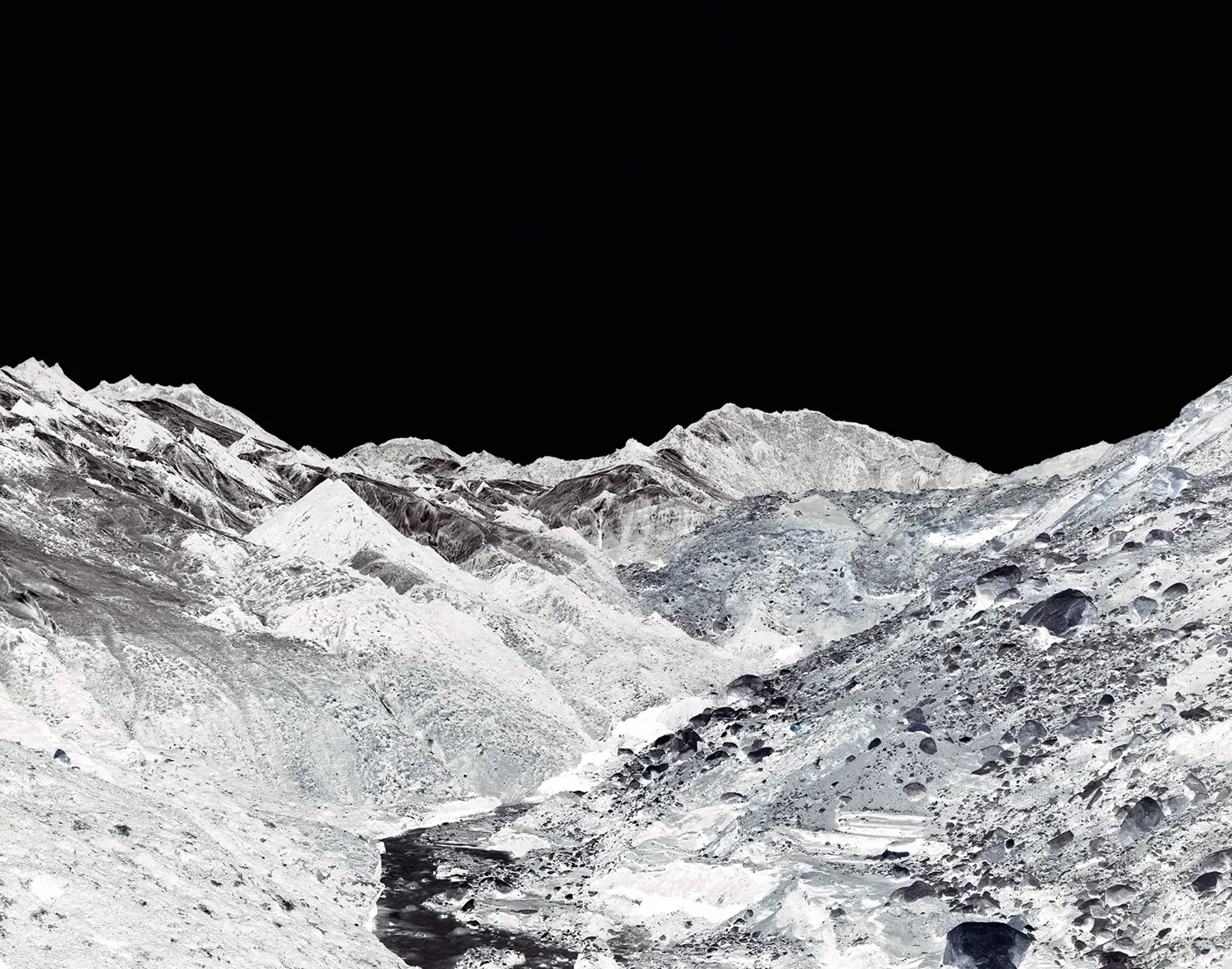 A black and white image of a rocky, snow-covered mountain range and a valley. The sky above is completely solid black. The image uses negative colours, making the snow look dark in places and the dark rocks look white.