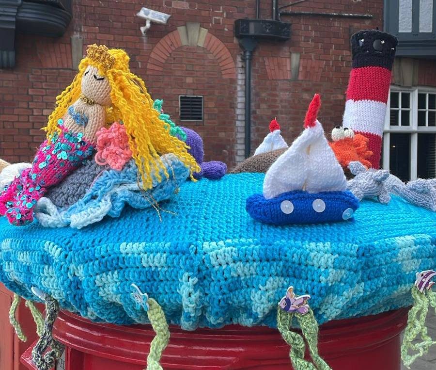Colourful knitted coastal creatures on top of a red post box