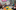 Parents and children sit in a circle around a colourful mat singing a song. One lady plays a ukelele