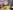 Parents and children sit in a circle around a colourful mat singing a song. One lady plays a ukelele